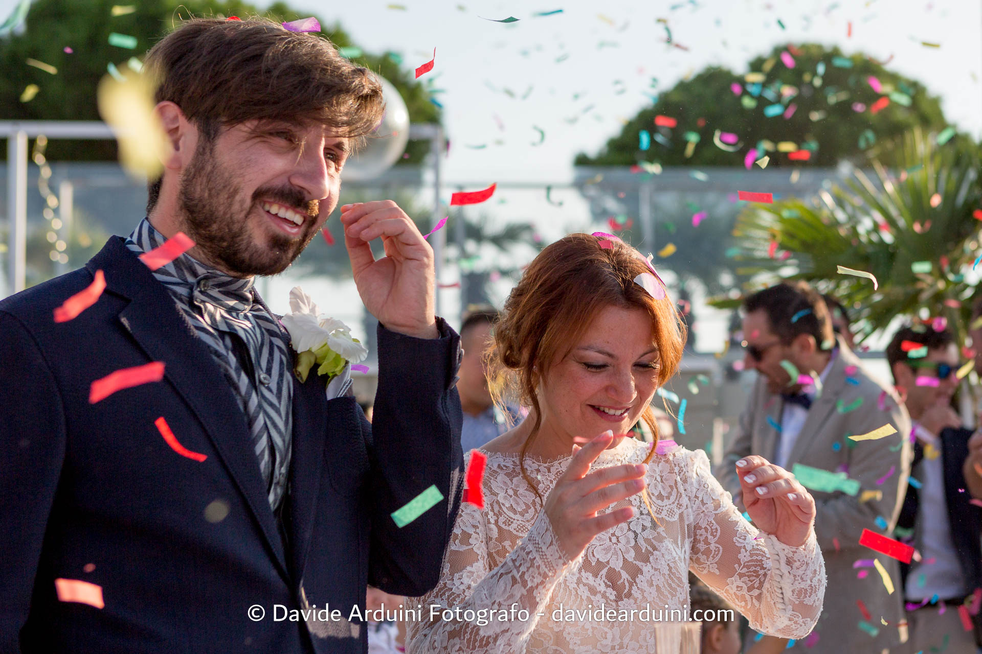 Una coppia di sposi sorridente mentre i coriandoli colorati cadono attorno a loro durante una celebrazione.