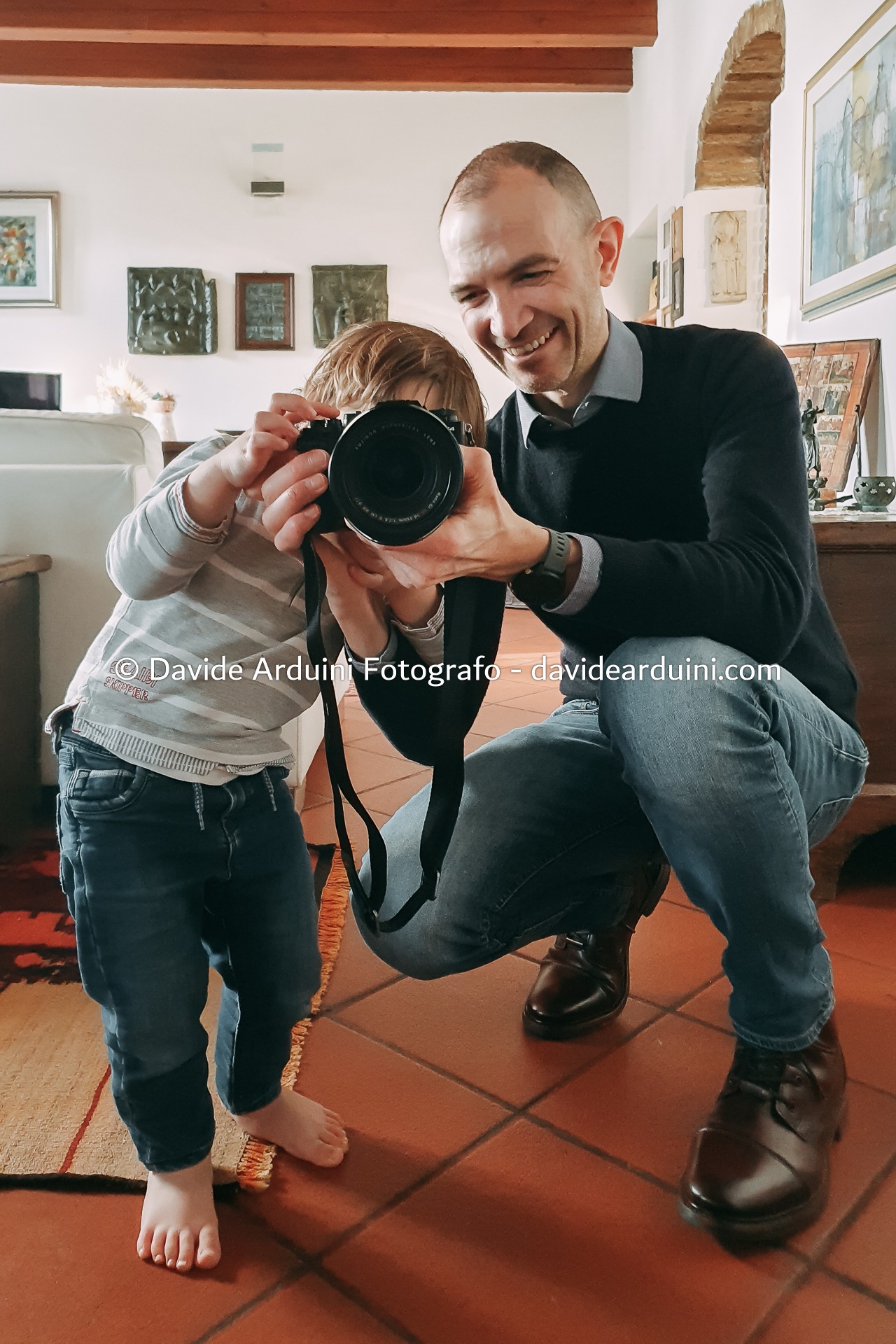 Davide Arduini Fotografo assieme a un bambino che tiene la sua macchina fotografica e lo fa giocare a fare il fotografo.