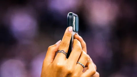 Mano che riprende con lo smartphone durante un evento, pubblico e luci di scena sfocati sullo sfondo