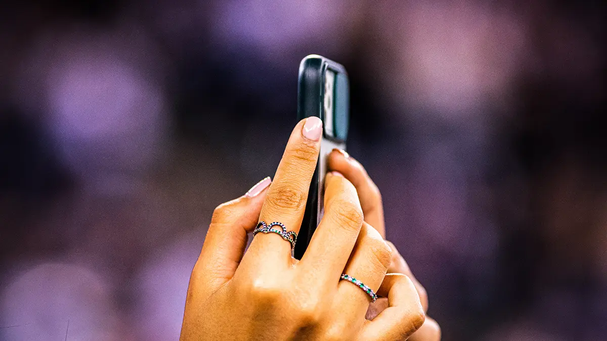 Mano che riprende con lo smartphone durante un evento, pubblico e luci di scena sfocati sullo sfondo