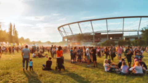 Folla sfocata a un evento all'aperto al tramonto, con uno stadio sullo sfondo