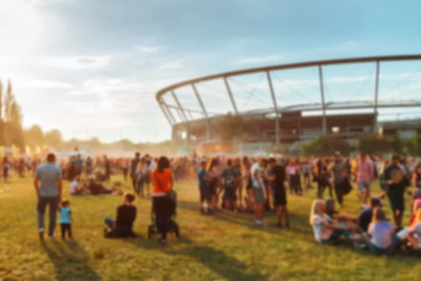 Folla sfocata a un evento all'aperto al tramonto, con uno stadio sullo sfondo